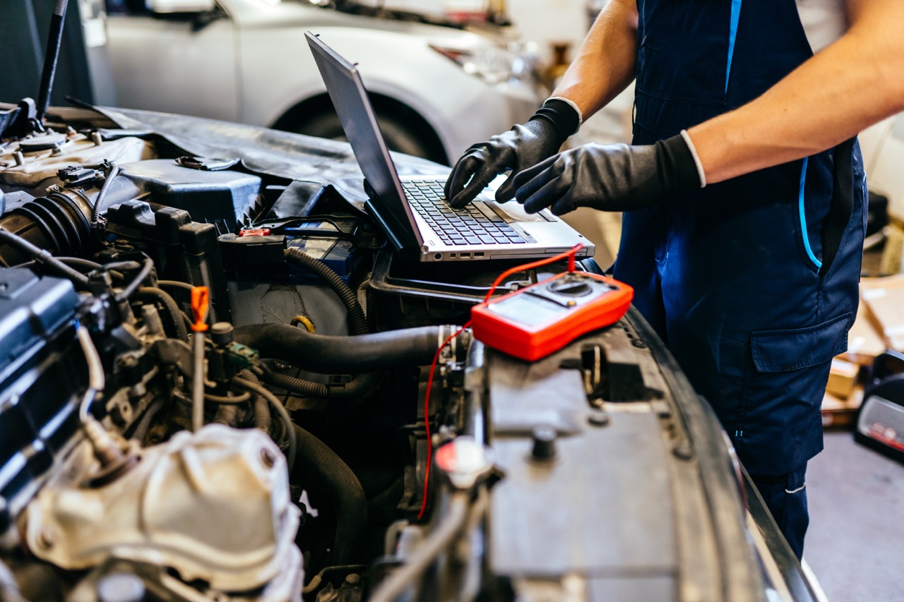 Car mechanic at work. Car an electrician using computer in auto repair shop. Close up.